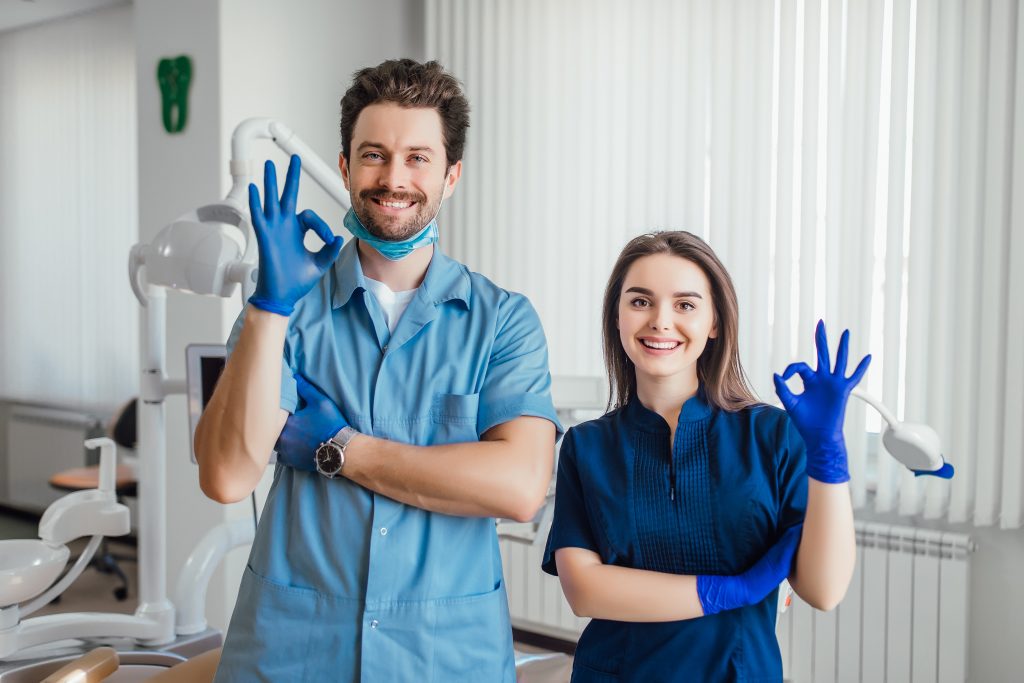 About - drafted 5 photo smiling dentist standing with arms crossed with her colleague showing okay sign